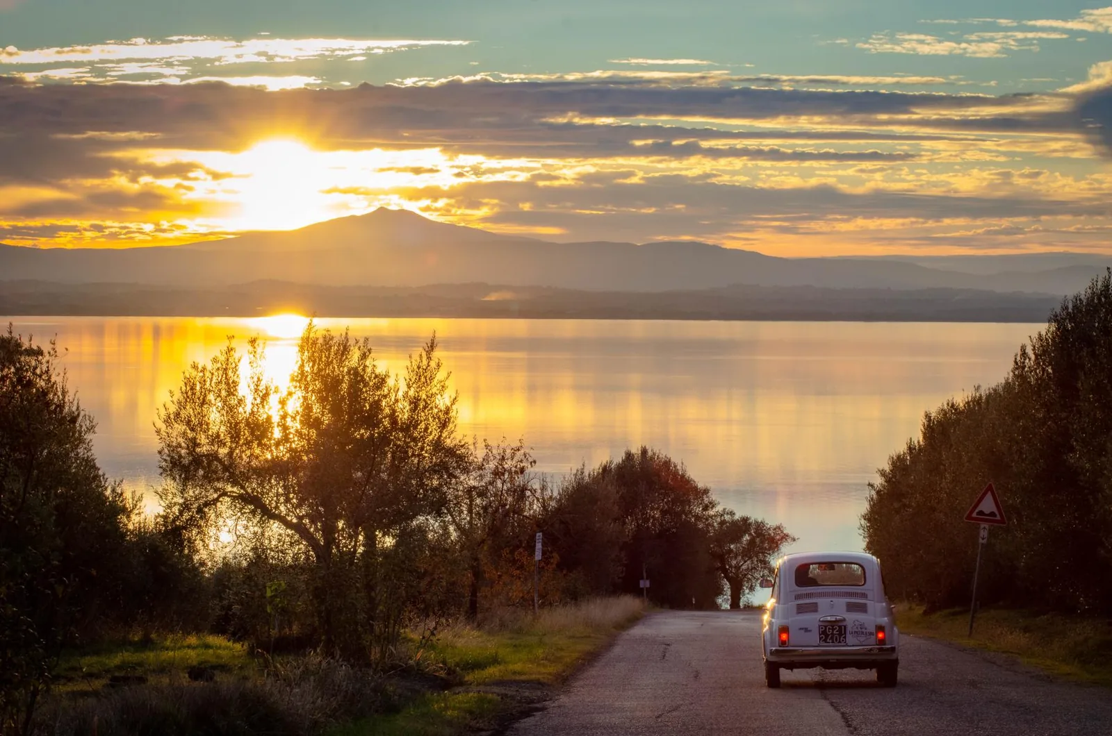 Historischer Fiat 500 auf einer Panoramastraße über dem Trasimenischen See bei Sonnenuntergang