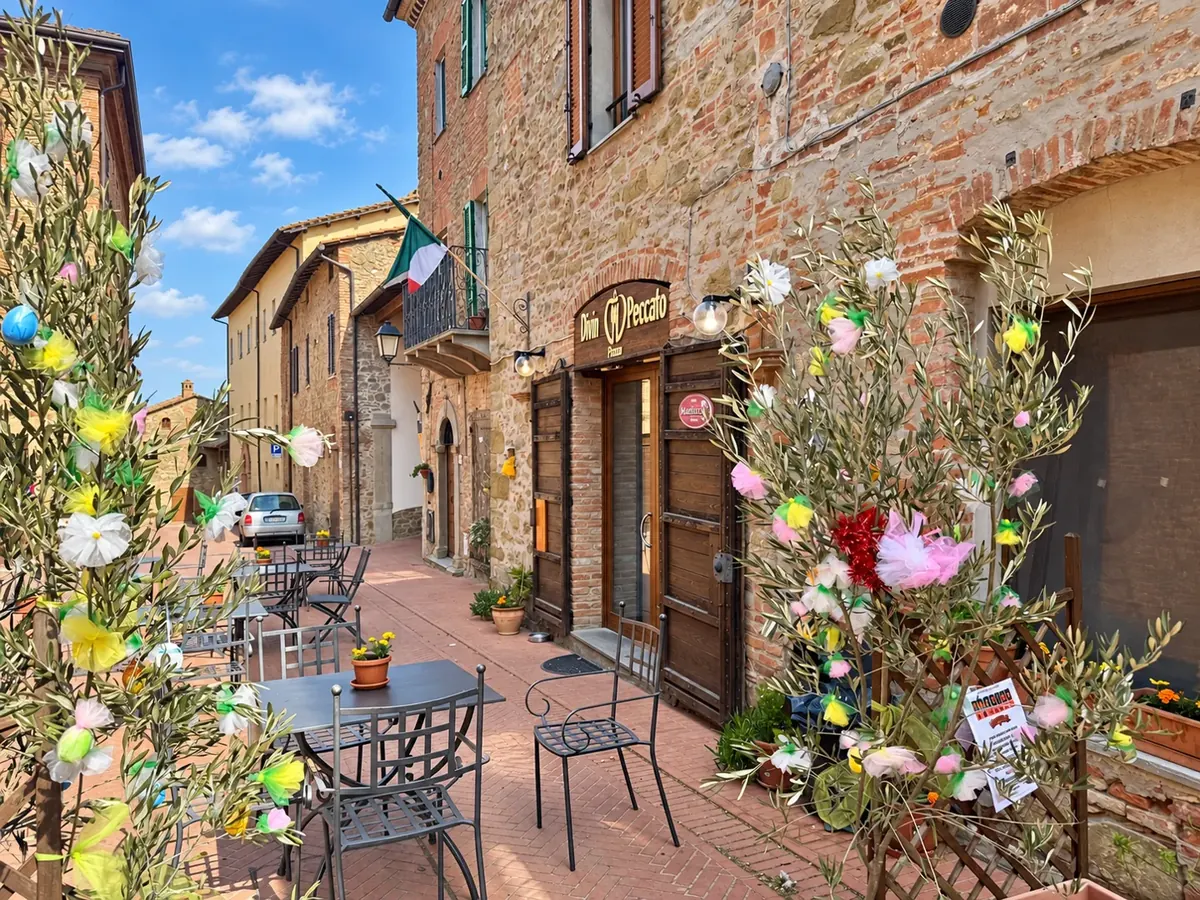 Entrée du Divin Peccato Cafè à Paciano, avec tables en terrasse et façade en pierre.