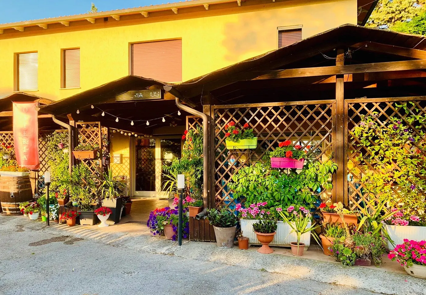 Entrée du restaurant Il Poderaccio, avec pergola en bois et pots fleuris