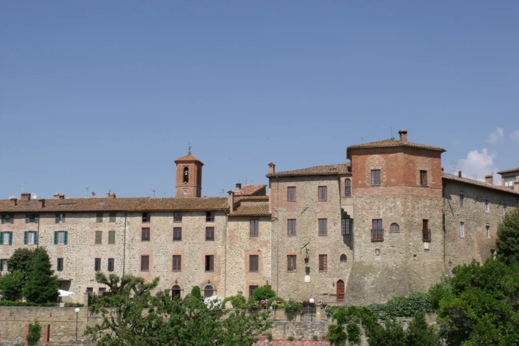 Steinhäuser und Glockenturm von Paciano zwischen Bäumen unter blauem Himmel