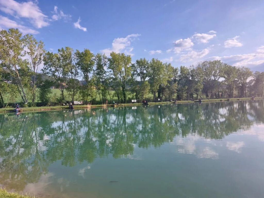 Alberi e nuvole riflessi nel lago di pesca sportiva della Fishing Accademy a Paciano