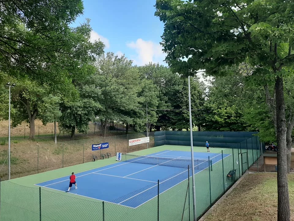 Due giocatori sul campo blu e verde del Tennis Paciano, circondato dagli alberi