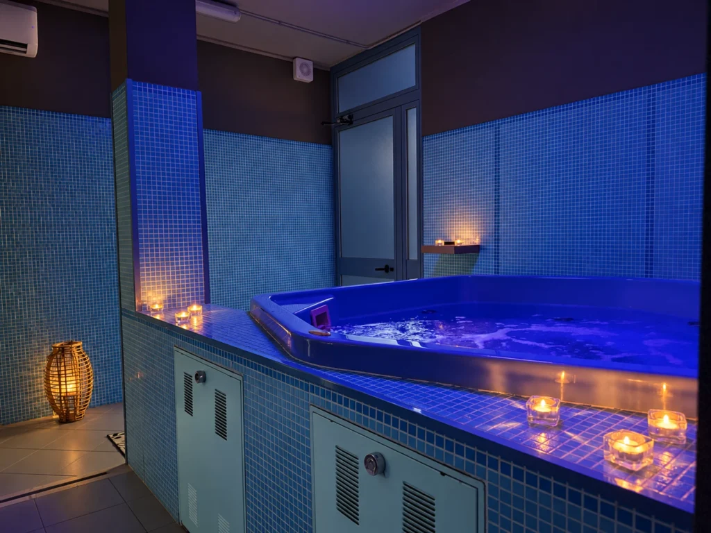 Vasca idromassaggio con mosaico azzurro e candele accese nel punto benessere di Tenuta Badia.