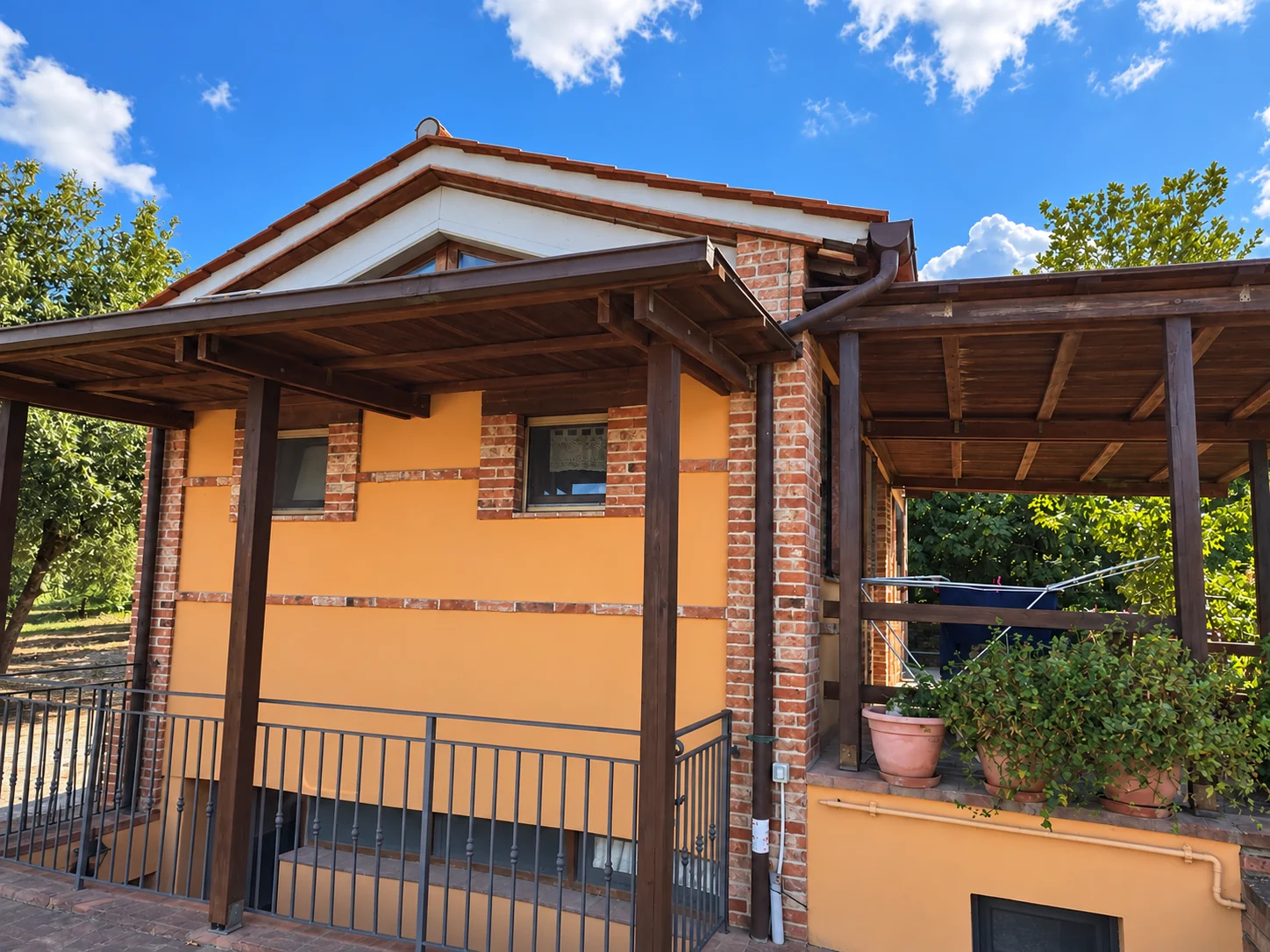 Esterno della Capanna alla Tenuta Badia di Paciano, con facciata color ocra, pilastri in mattoni e portico in legno