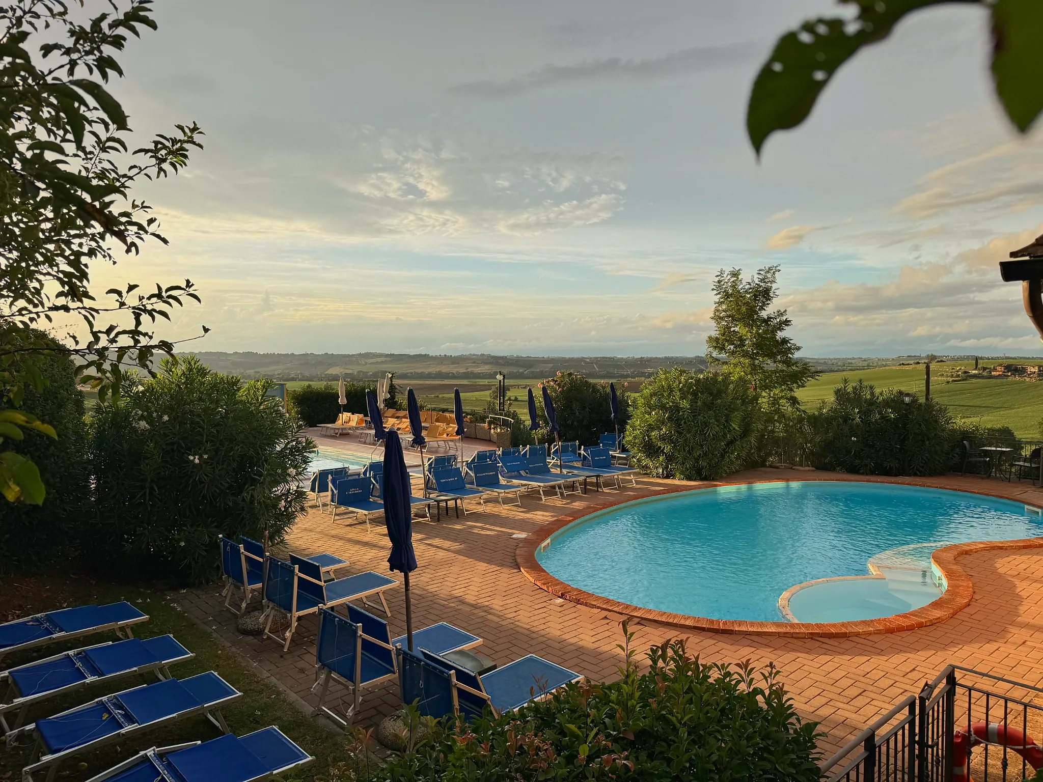 Piscina curva di Tenuta Badia con lettini blu e vista aperta sui campi e sulle colline umbre.