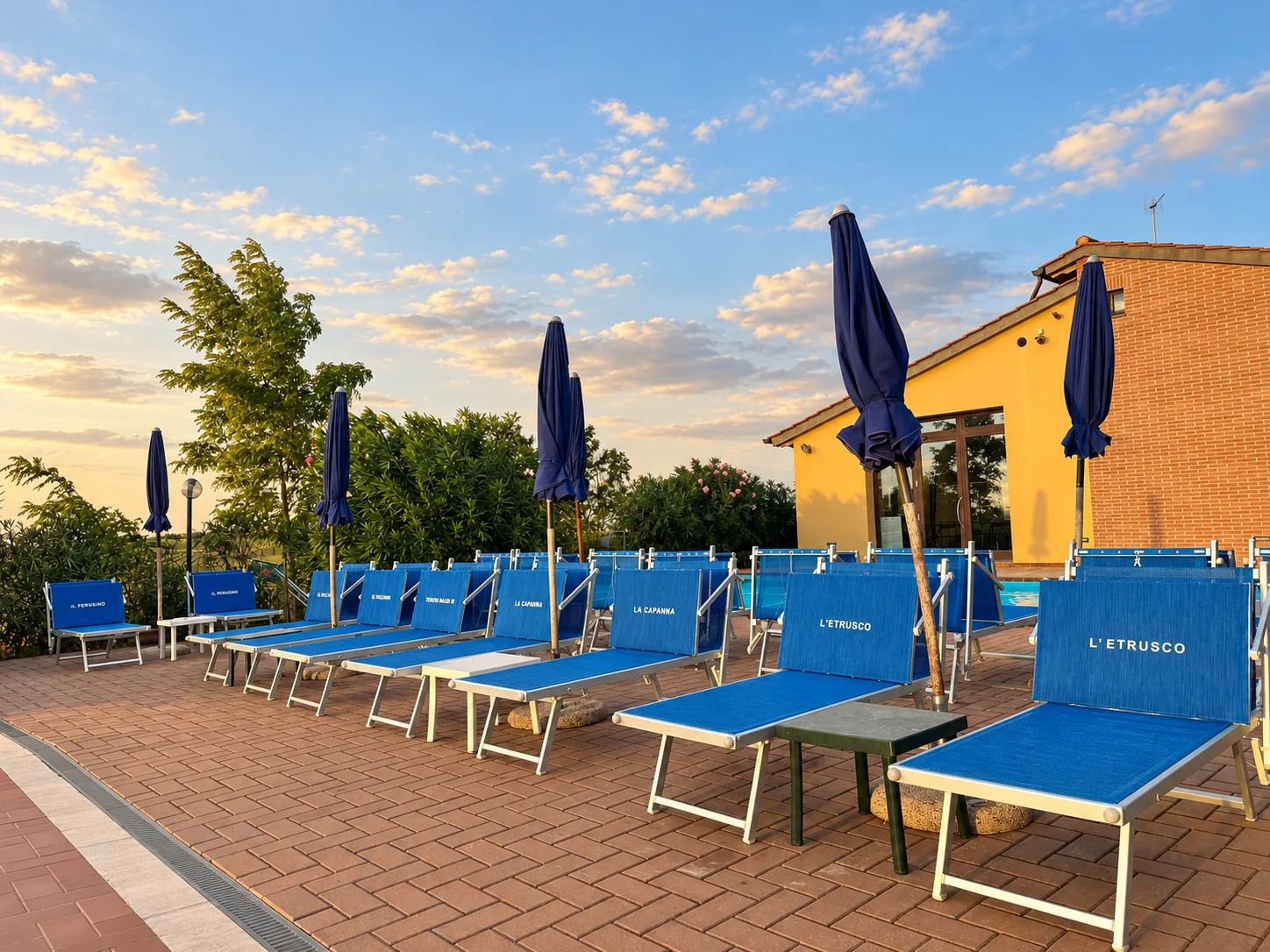 File di lettini blu personalizzati e ombrelloni chiusi nel solarium di Tenuta Badia, accanto all’edificio giallo.