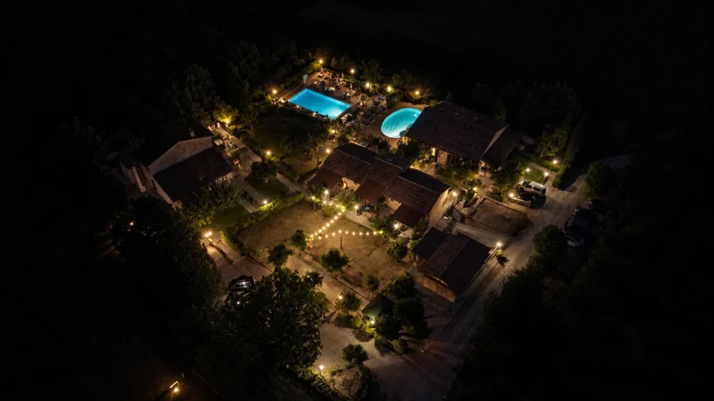 Veduta aerea notturna di Tenuta Badia, con due piscine azzurre illuminate, edifici e luci calde nel giardino.