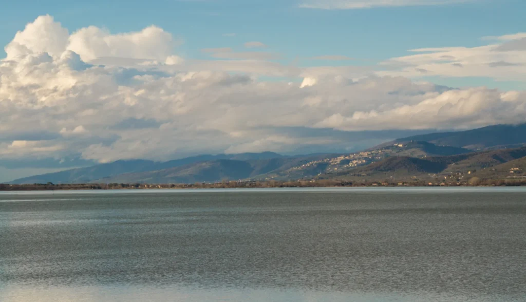 Trasimenischer See unter Wolken mit den Hügeln von Cortona am Horizont