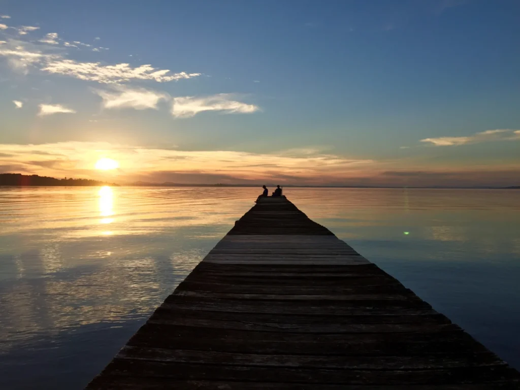 Pontile di legno sul Lago Trasimeno al tramonto, con due persone in fondo al molo