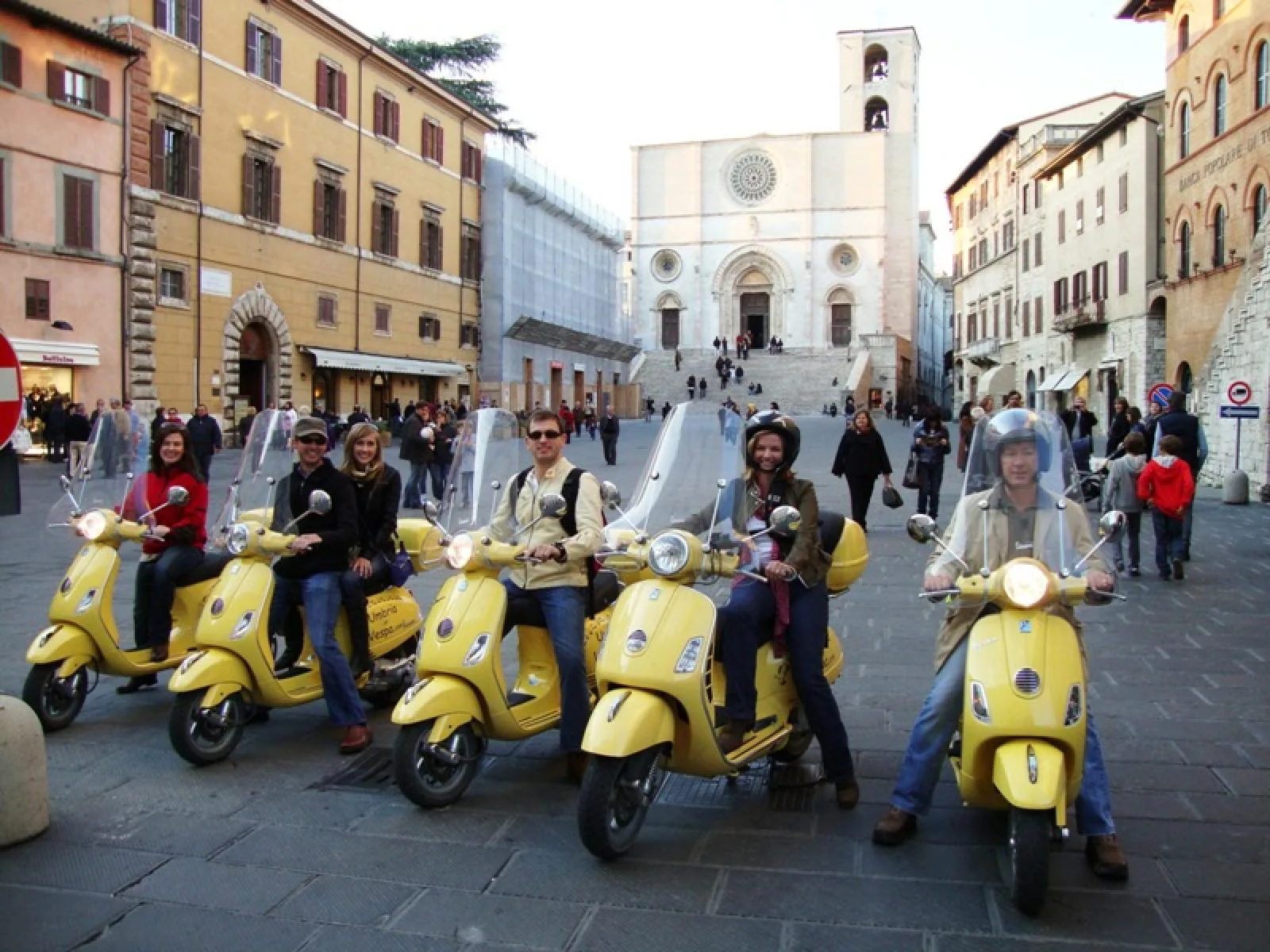Gruppo di viaggiatori su Vespe gialle nella piazza di un borgo umbro
