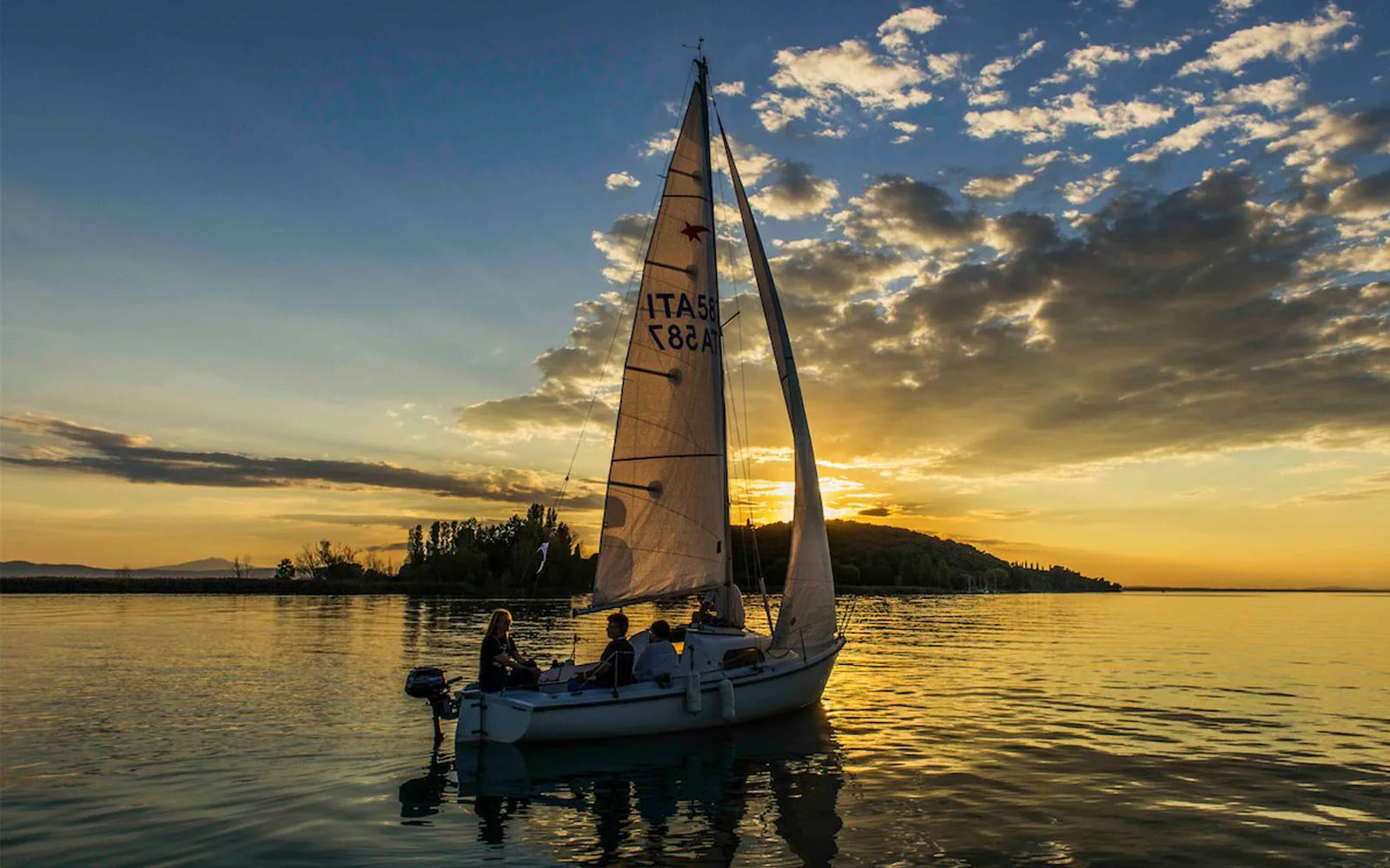 Segelboot mit Besatzung auf dem Trasimenischen See bei Sonnenuntergang